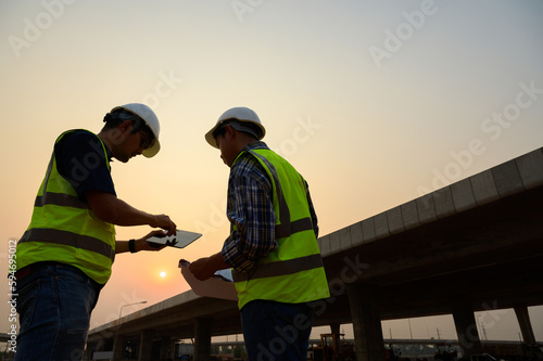 Asian Two civil engineer specialists examining trades at road construction site, industrial building construction site. Concrete skyscraper of road construction