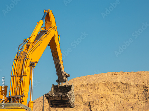 An orange excavator fills up the earth in the body of a construction dump truck. Excavator with bucket and dump truck  while working on the background of the blue sky close-up.