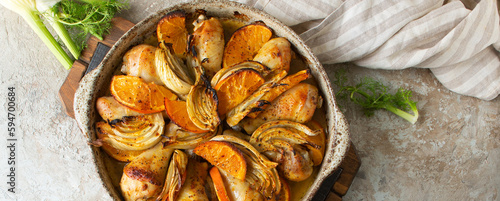 ceramic dish with baked chicken legs with fennel and orange on the table