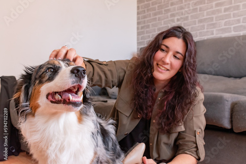 Young woman on the ground smiling while petting her dog. Australian Sheepdog.
