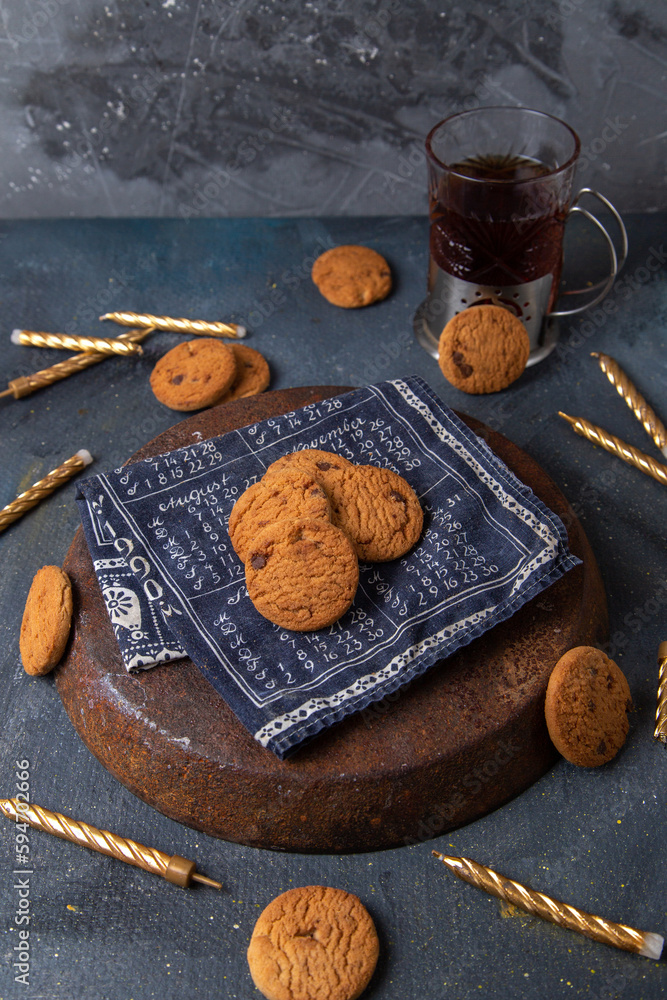 front view delicious chocolate cookies with cup of tea and candles on the dark-grey background cookie biscuit sweet sugar tea front view delicious chocolate cookies with cup of tea and candles on the dark-grey background cookie biscuit sweet sugar tea