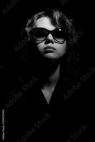 Fashionable portrait of a young woman in sunglasses in contrast lighting.
