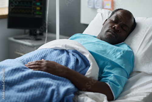 African American unconscious patient lying on bed in hospital ward with monitor checking his heartbeat in background photo