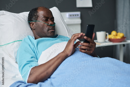 African American elderly patient using smartphone while lying on bed in hospital