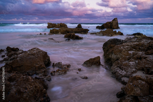 Purple Dawn sky over long exposure waves on rocky shoreline