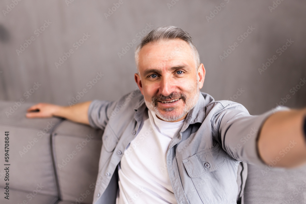 Fototapeta premium middle-aged man in his sofa takes a picture in selfie at home