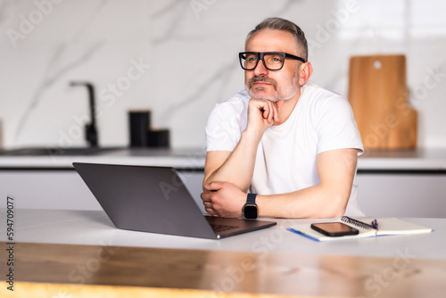 Handsome man using a laptop pc in the kitchen. Working from home