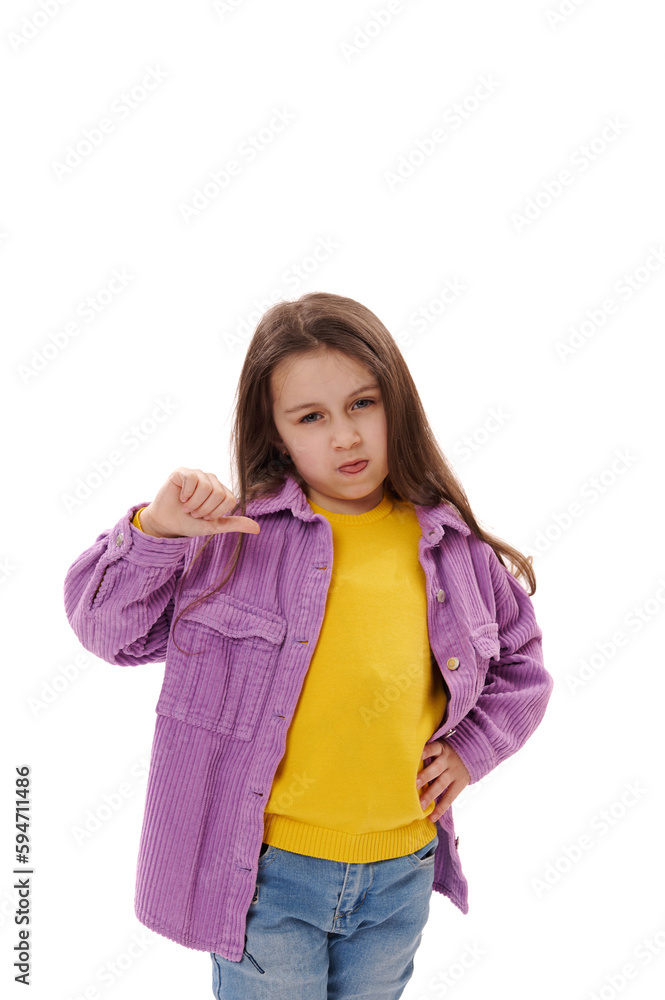 Mischievous 5-6 years little child girl gestures with thumbs down, makes faces, grimaces, shows her tongue looking at camera, expressing misunderstanding and disagreement, isolated on white background Mischievous 5-6 years little child girl gestures with thumbs down, makes faces, grimaces, shows her tongue looking at camera, expressing misunderstanding and disagreement, isolated on white background
