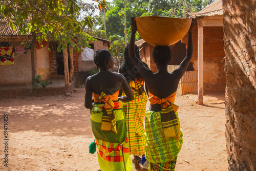 Black women carrying water in basin in village photo