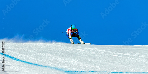 Billede på lærred male ski racer on alpine skiing track downhill, snowy slope on blue sky backgrou