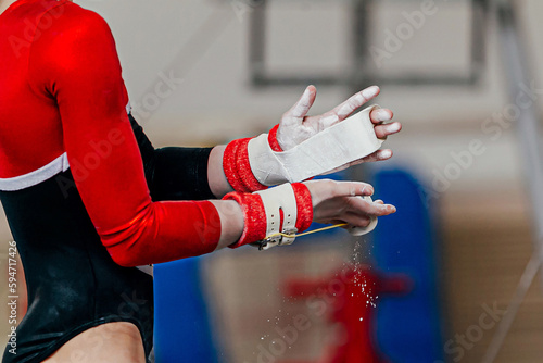 close-up hands female gymnast in gymnastics grips in gym chalk, uneven bars performing