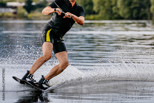 Photography male athlete wakesurfing behind motorboat on pond, extreme summer water sports
