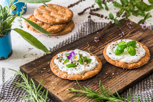 Round crispbread with herbal cream cheese and fresh herbs on a wooden board