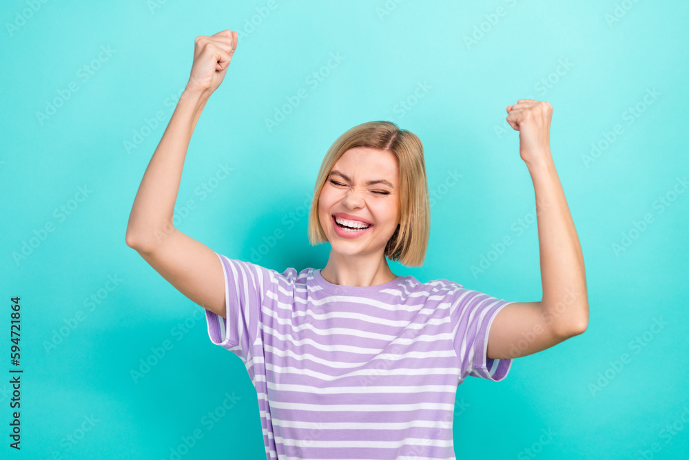 Portrait of optimistic woman with short haircut dressed stylish t-shirt raising fist up scream yeah isolated on teal color background Portrait of optimistic woman with short haircut dressed stylish t-shirt raising fist up scream yeah isolated on teal color background
