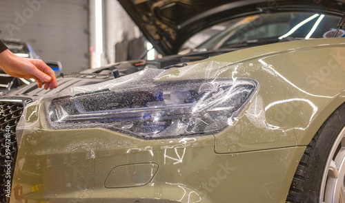 The process of installing a protective polyurethane film for paint on the front headlight of a car. PPF is a polyurethane film that helps protect glass and metal from scratches. Selective focus.   photo