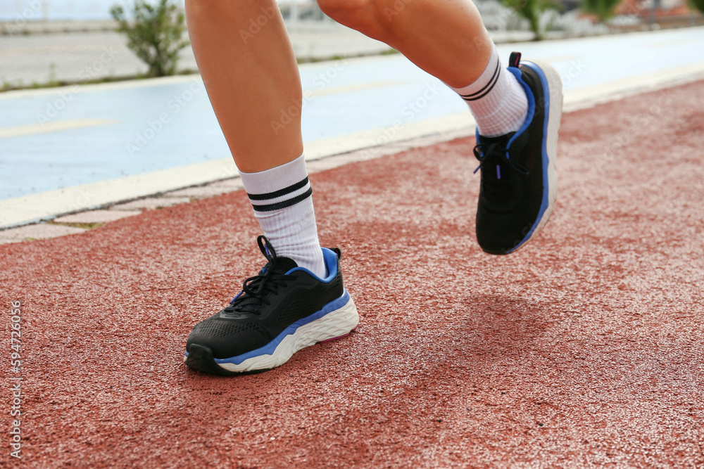 Cropped shot of female athlete wearing textile cruelty free shoes and jogging on a synthetic surface of running track. Close up, copy space, background.