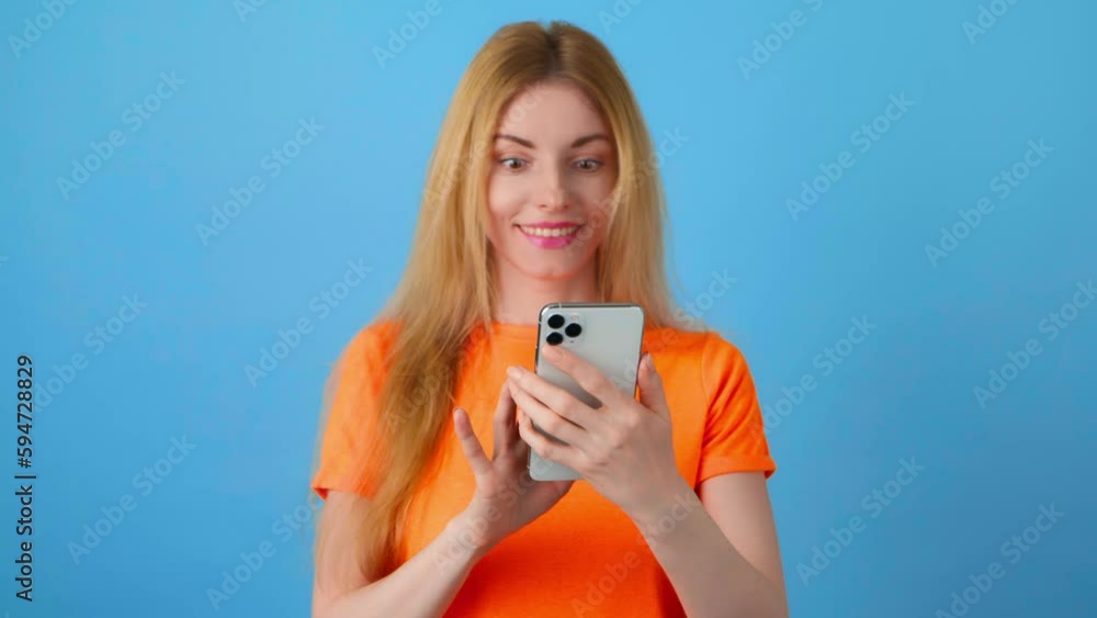 Surprised young woman pointing at mobile phone. Wow! Lady amazed excited with smartphone for social media, online streaming, news and internet, surprise face. Studio shot isolated on blue background Surprised young woman pointing at mobile phone. Wow! Lady amazed excited with smartphone for social media, online streaming, news and internet, surprise face. Studio shot isolated on blue background