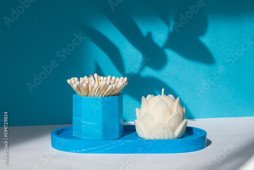 A lotus candle and a glass with matches on a blue-white background.