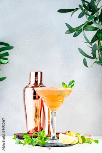 French daiquiri alcohlic cocktail with cognac, syrup, lemon juice, mint and ice in glass garnished with brown sugar rim. Gray background, bar tools photo