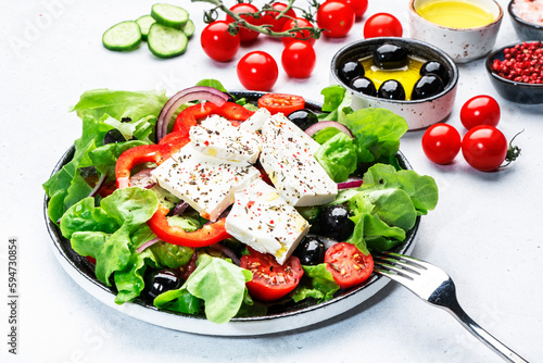 Greek salad with feta cheese, kalamata olives, cherry tomato, yellow paprika, cucumber and onion, healthy mediterranean diet food, low calories eating. White table background, top view