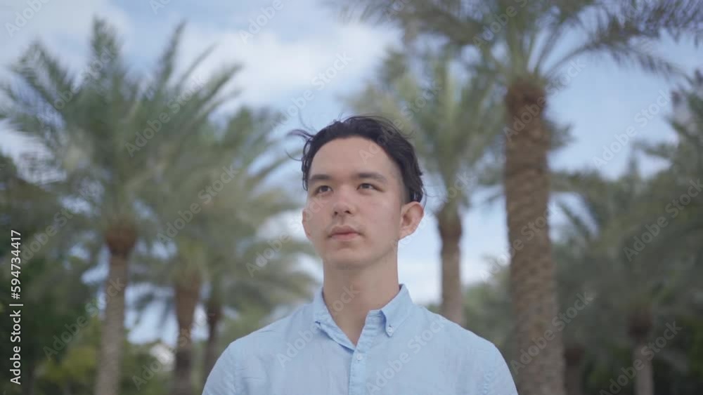 Smiling young Asian man. A handsome young Asian stands against the backdrop of buildings and palm trees. Spring concept. Foreground. Smiling young Asian man. A handsome young Asian stands against the backdrop of buildings and palm trees. Spring concept. Foreground.