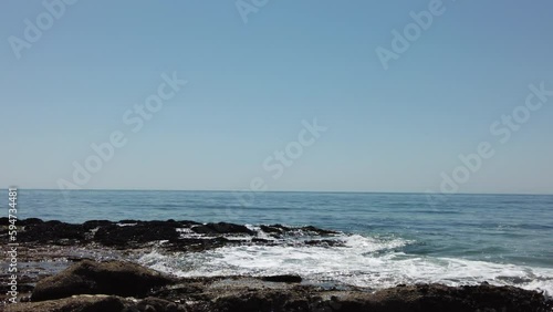 Whitewater waves crashing over rocks near the shoreline of the Pacific Ocean