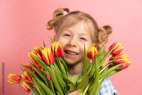 a small blonde on a pink background with a bouquet of red tulips in her hands, smiling. close-up portrait. holiday concept