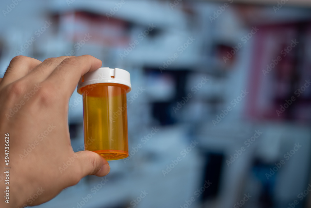 Hand holding an empty orange bottle of medicine in laboratory background Hand holding an empty orange bottle of medicine in laboratory background