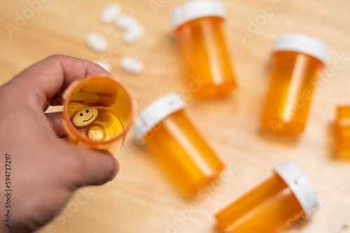 Top view of a hand holding a bottle with only a pill with drawn happy face and pills and empty bottles in background, anti-depressive concept