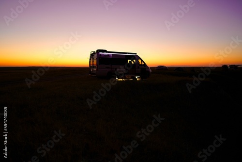Silhouette of a small camper parked in a beautiful open landscape at sunset