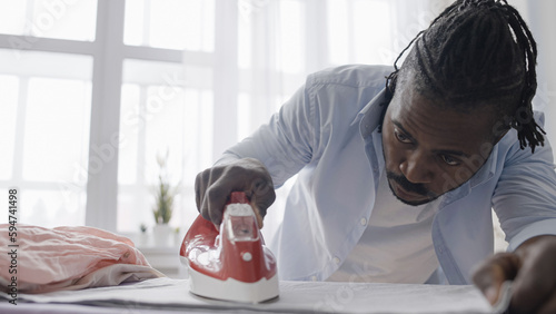 Fényképezés African American man perfectionist meticulously ironing clothes, household chore