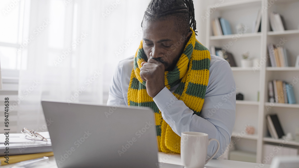 An ill office worker is coughing and drinking warm tea while typing on