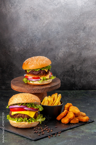 Mouth-watering delicious sandwiches fries chicken nuggets on black board fries pepper on dark gray blurred background