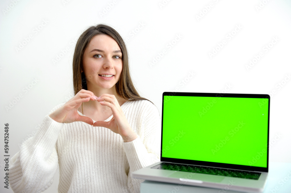 Young woman speak with friends on video call and shows heart with hands on camera from home office. Virtual party meeting team teleworking. Remote conference Computer green screen view. Young woman speak with friends on video call and shows heart with hands on camera from home office. Virtual party meeting team teleworking. Remote conference Computer green screen view.