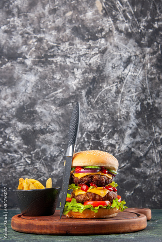 Tasty homemade sandwich tomatoes fries gray knife on wooden cutting board on dark color background with free space in vertical view photo