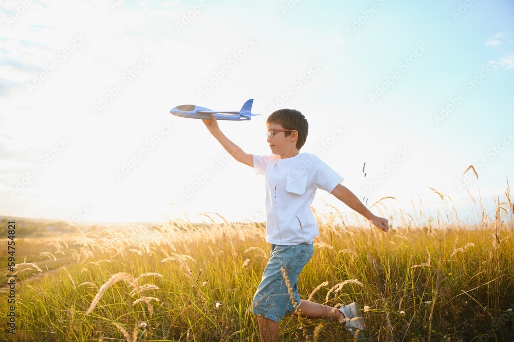 The kid runs with a toy plane. Son dreams of flying. Happy child, boy, runs on the sun playing with a toy airplane on the summer field The kid runs with a toy plane. Son dreams of flying. Happy child, boy, runs on the sun playing with a toy airplane on the summer field