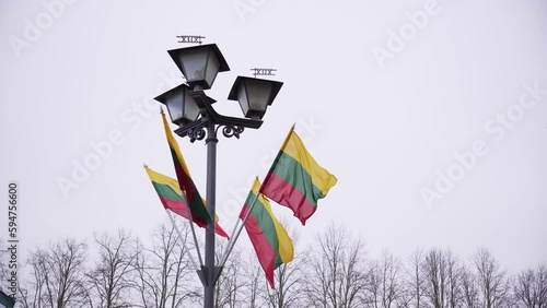 Flag of Lithuania fluttering in the wind on the street lantern against the cloudy sky photo