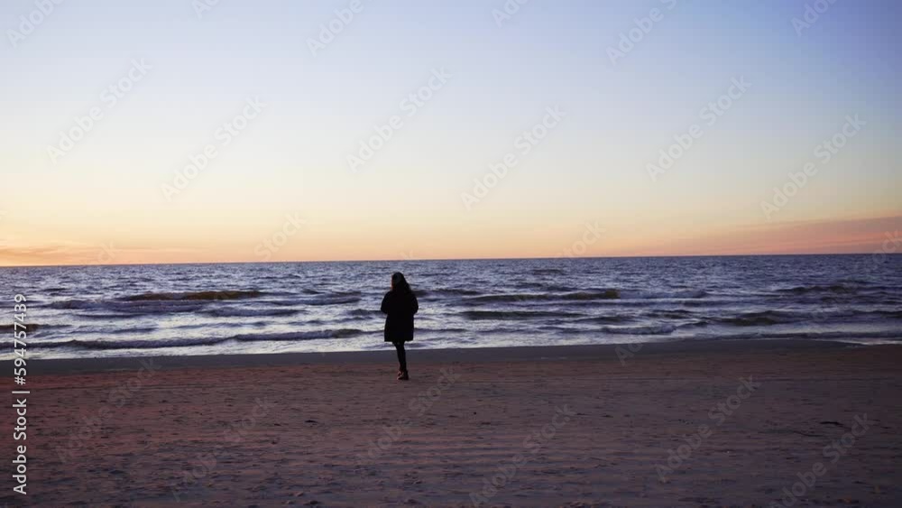 Silhouette of a female walking on the sandy shore with the golden sunset and sea in the background Silhouette of a female walking on the sandy shore with the golden sunset and sea in the background