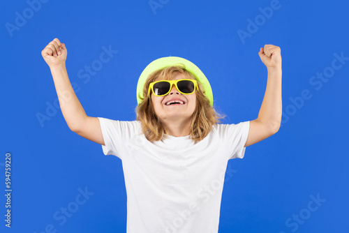 Funny summer fashion kid boy. Fashion portrait of kid in summer hat, t-shirt and sunglasses on blue studio isolated background.