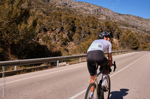 Fit man cyclist wearing white cycling jersey and helmet training on road bicycle on empty mountain road.Training for competition.Sport motivation.Alicante region in Spain.