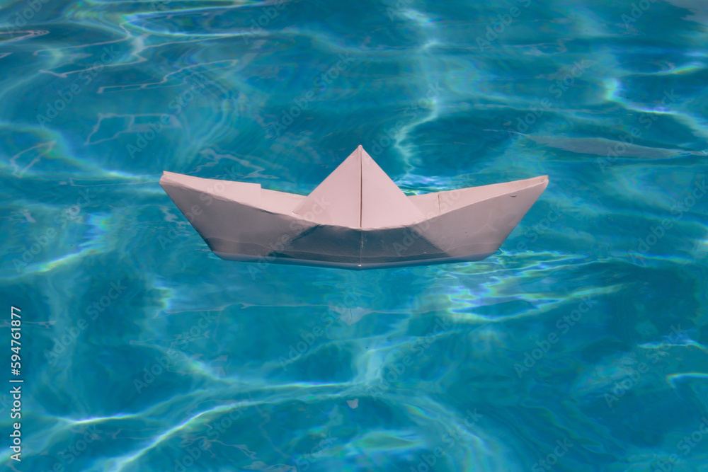 White paper boat into the clear sea water. Blue water background.