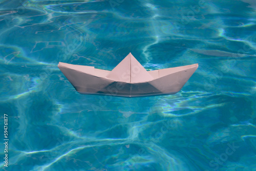 White paper boat into the clear sea water. Blue water background. © Volodymyr