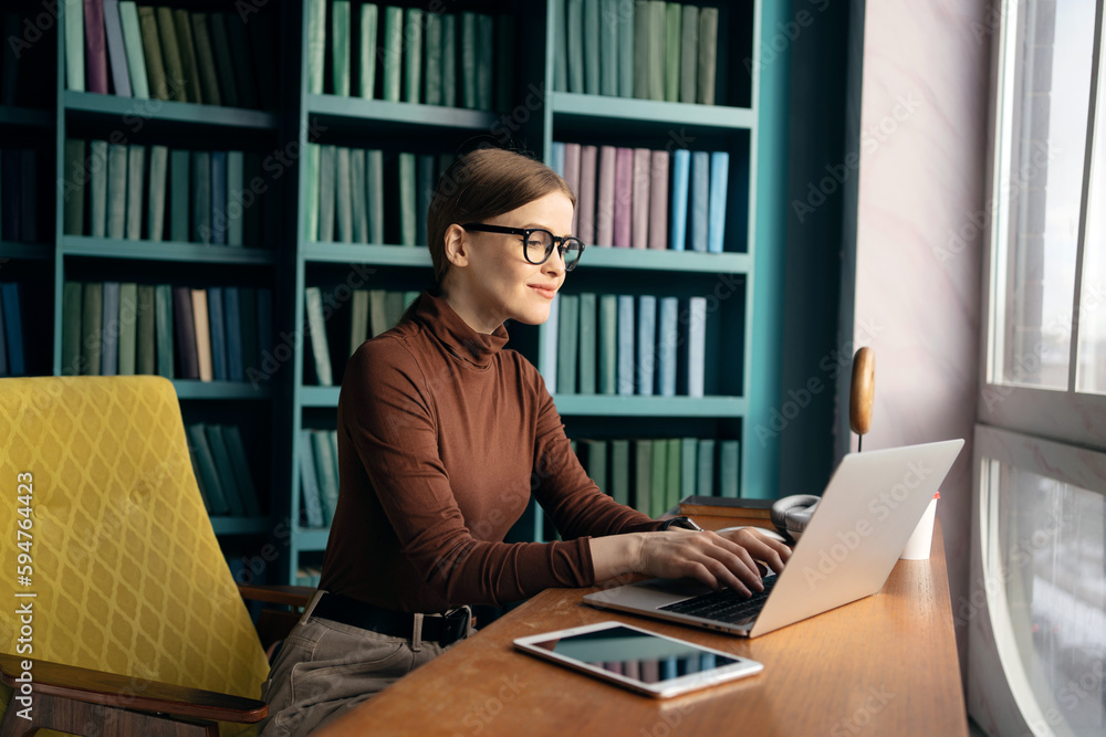 A woman sits at a desk in front of a bookcase that a writer using laptop A woman sits at a desk in front of a bookcase that a writer using laptop