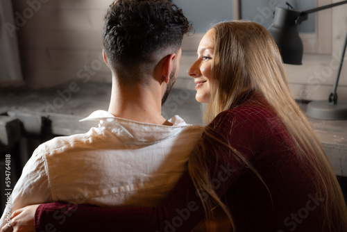 A girl and a guy sit in a room near a table and look at each other with love