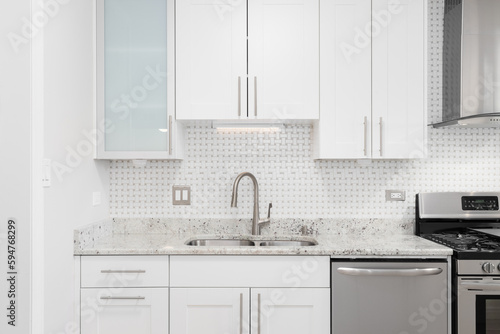 A beautiful white kitchen detail shot with a tiled backsplash, white cabinets, stainless steel appliances, and marble countertop.
