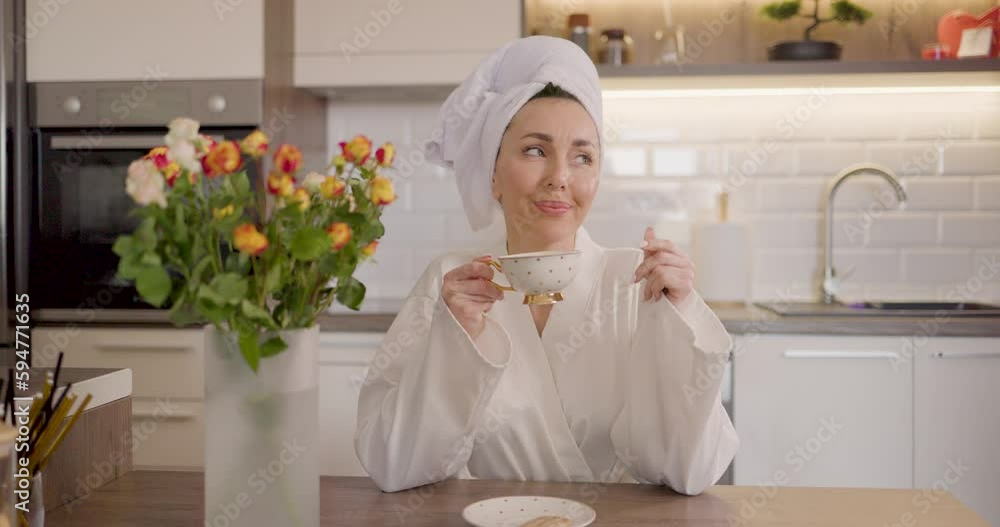 An attractive woman in bathrobe enjoying morning coffee and biscuit while relaxing in the kitchen at home. An attractive woman in bathrobe enjoying morning coffee and biscuit while relaxing in the kitchen at home.