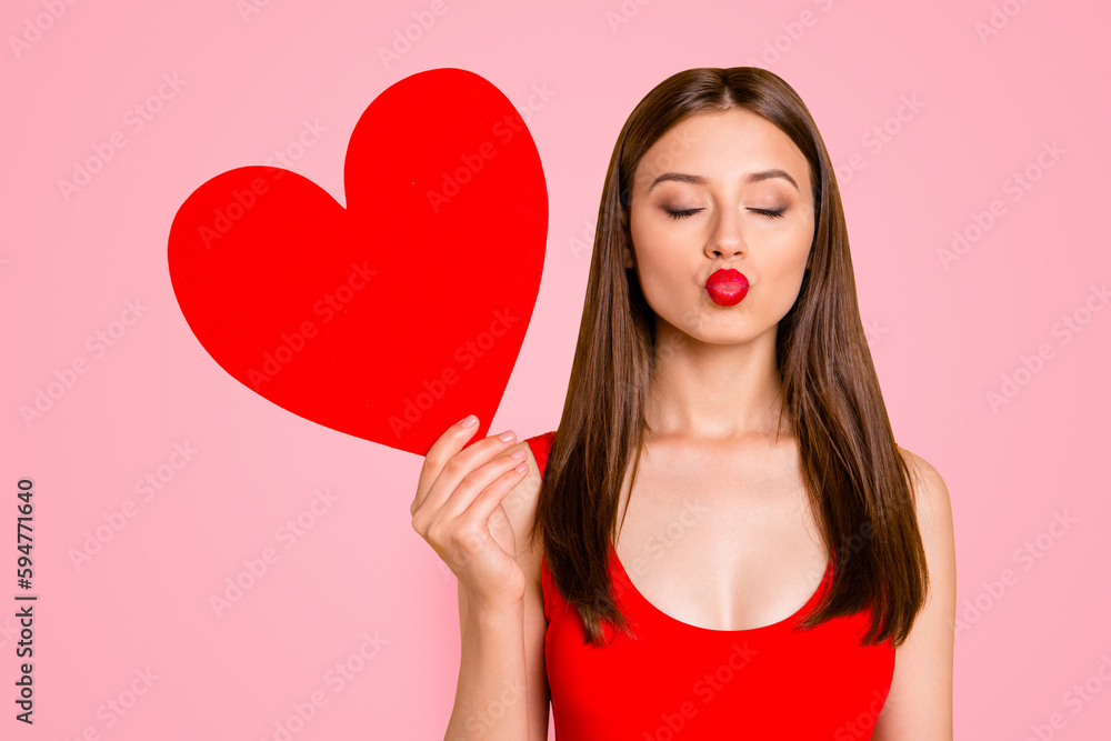 Portrait of charming woman with big paper carton red heart in hand waiting a kiss isolated on yellow vivid background Portrait of charming woman with big paper carton red heart in hand waiting a kiss isolated on yellow vivid background