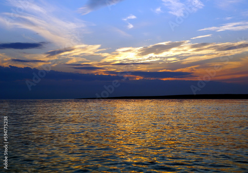 Big sea with small peace of land on the horizon with colorful sky above