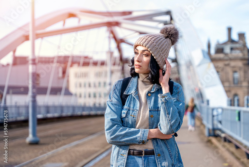 a young woman in a denim jacket is talking on the phone and waiting for a tram at the stop Lifestyle photo