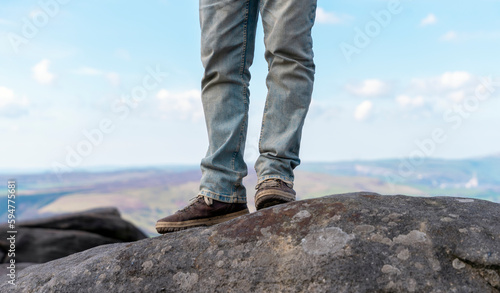 man in special boots walking in the mountains reaching the destination and on the top of mountain in Peak District against blue cloudy sky on sunny day Travel Lifestyle concept